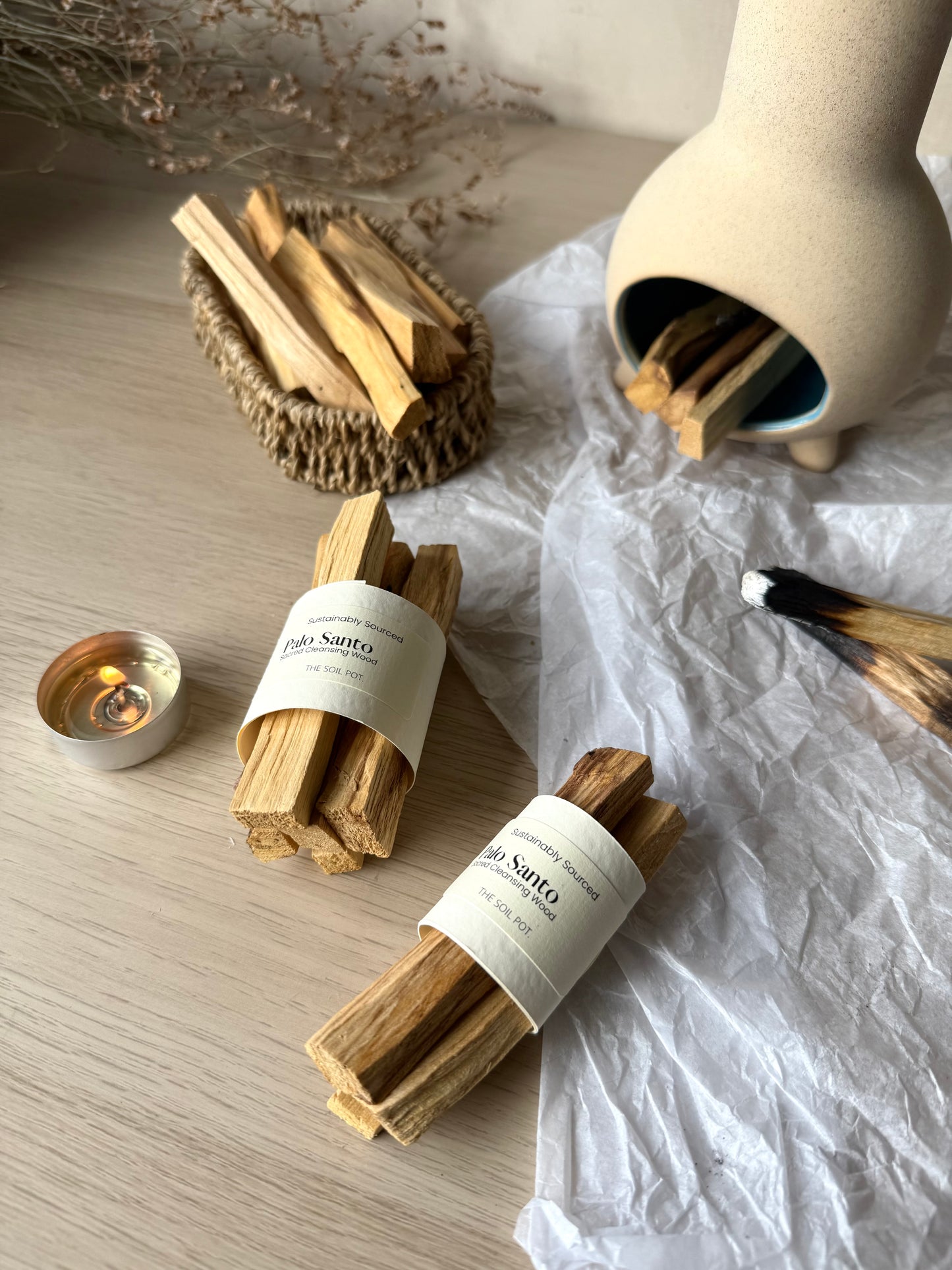 Packs of palo santo sticks with labels on a light surface with a candle and ceramic container.