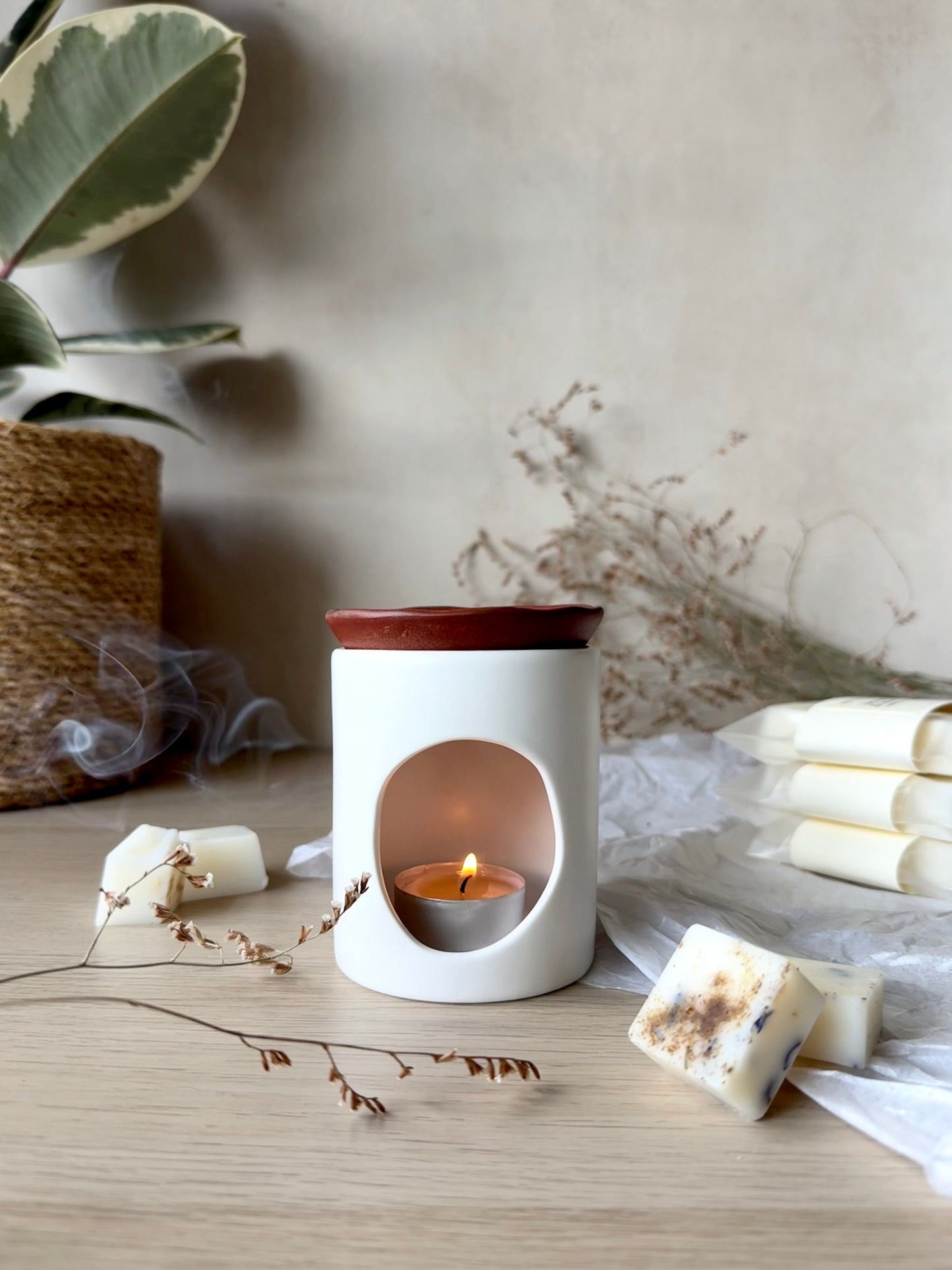 White wax melter with a small candle inside on a wooden surface with decorative elements.