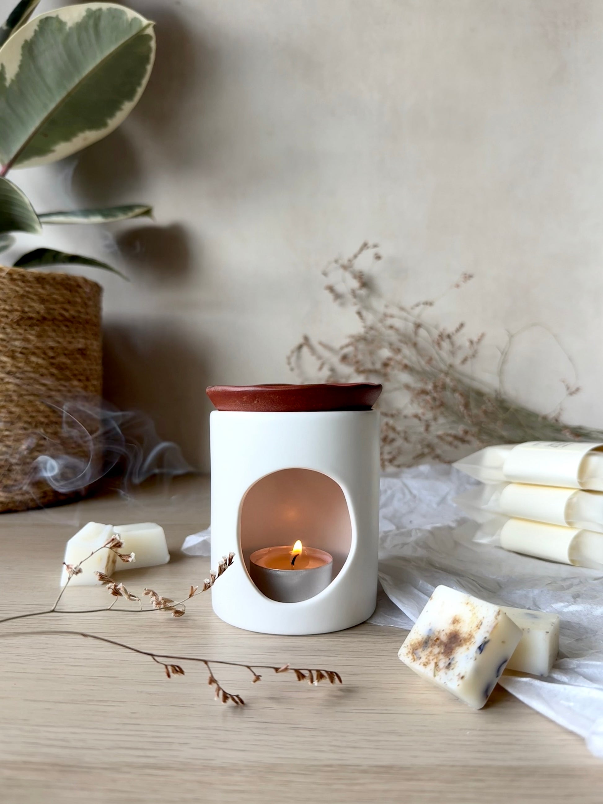 White wax melter with a small candle inside on a wooden surface with decorative elements.