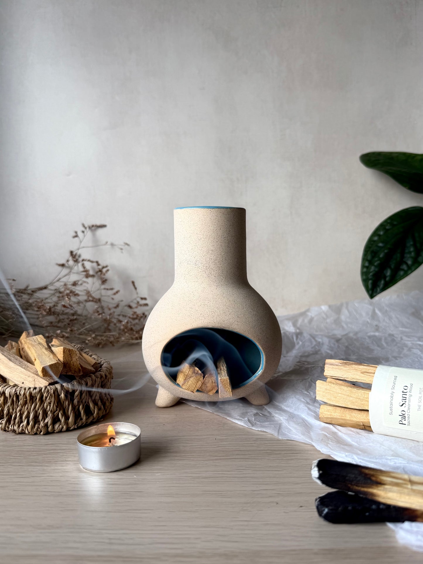 Ceramic chiminea with palo santo on a wooden surface, surrounded by minimal decor.