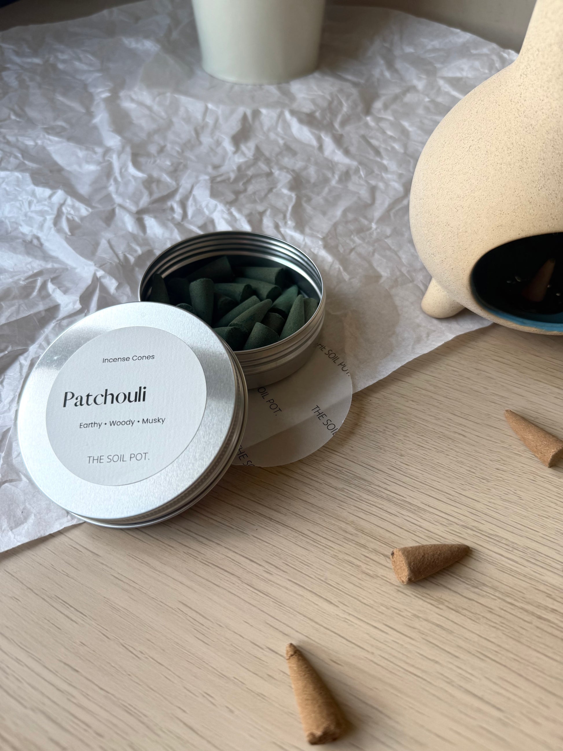 Patchouli incense cones in a container on a wooden surface with cones scattered around.